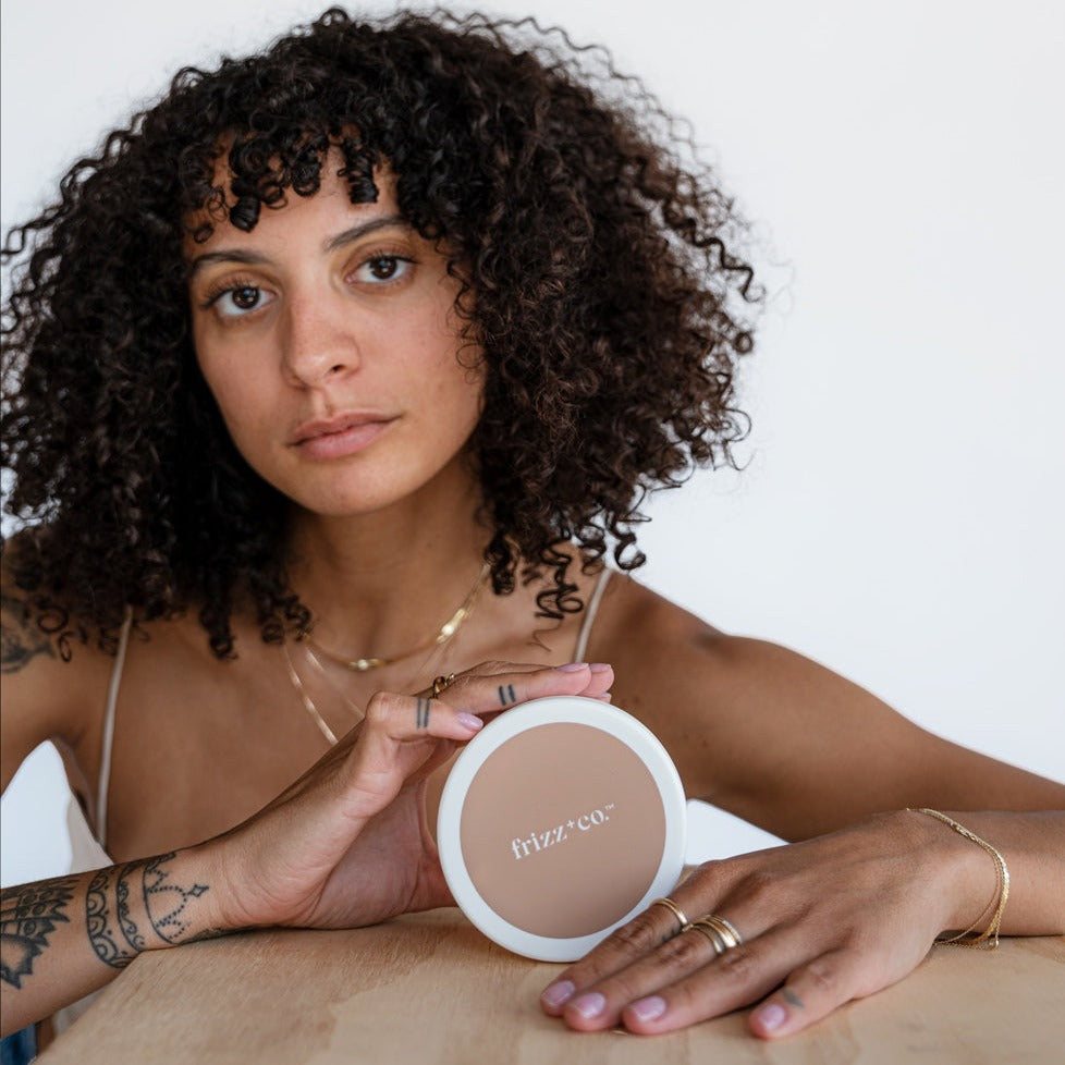 Close up of a woman with 3b hair holding the Repairing Hair Mask.